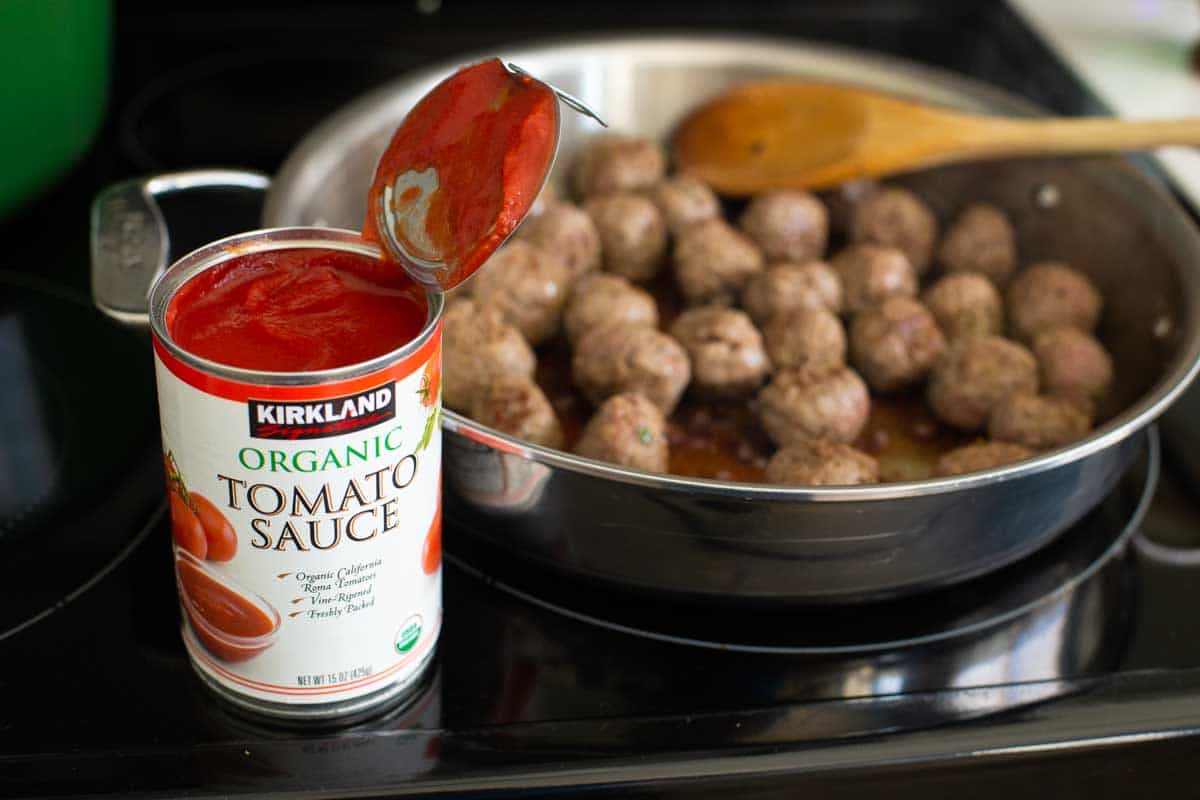 A can of tomato sauce sits next to the meatballs skillet.