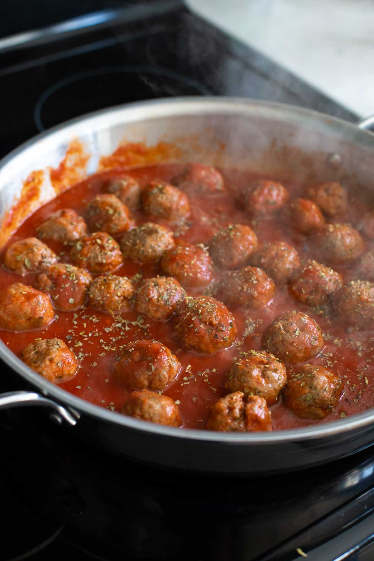 The meatballs are cooking in the tomato sauce and steam is rising up.