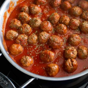 A skillet filled with meatballs and tomato sauce sprinkled with Italian herbs.