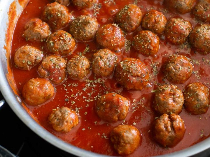 A skillet filled with meatballs and tomato sauce sprinkled with Italian herbs.