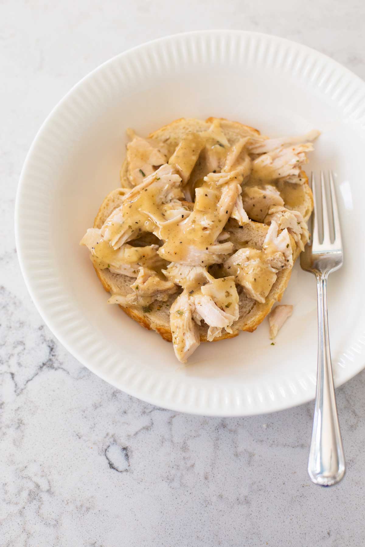 A bowl filled with an open face turkey sandwich has a fork on the side.