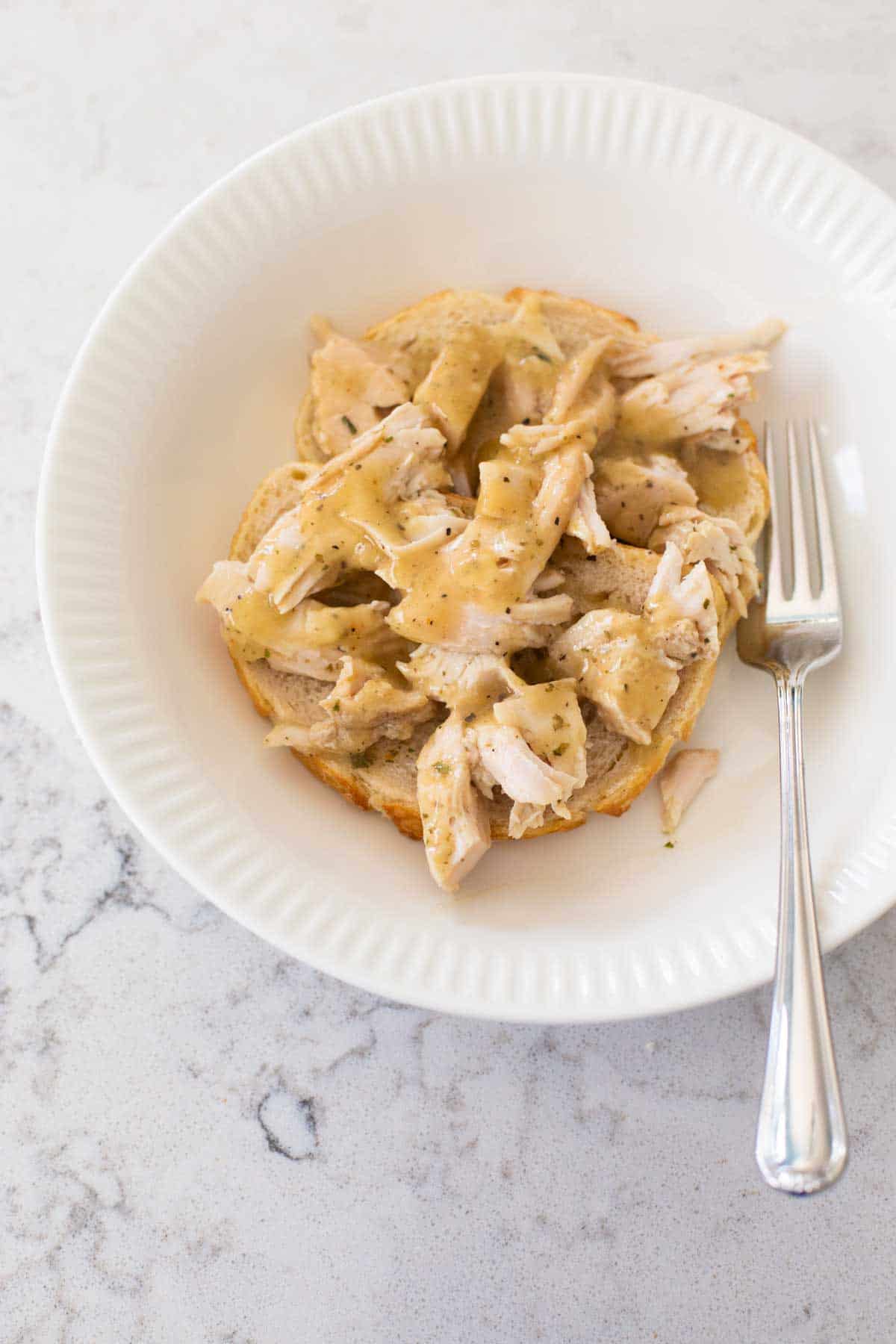 A bowl filled with an open face turkey sandwich has a fork on the side.