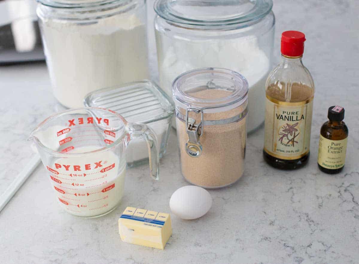 The ingredients to make orange rolls in a bread machine are on the counter.