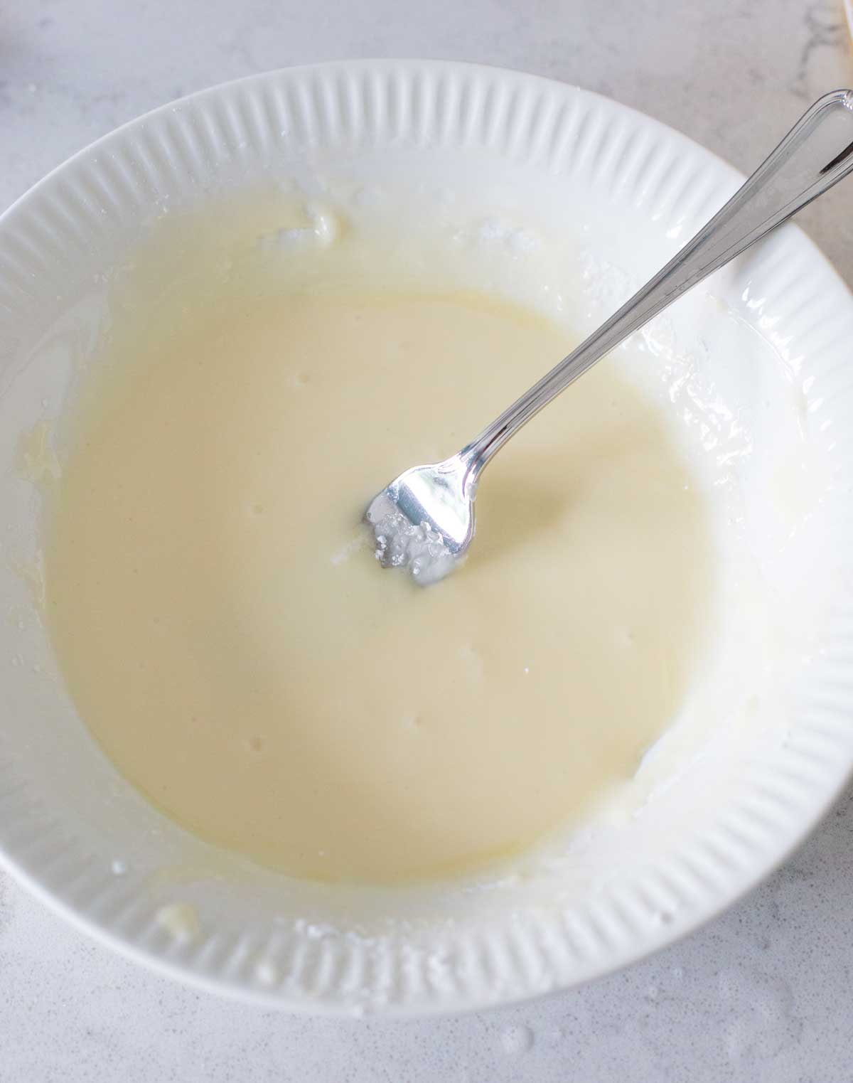 The orange icing has been whisked together with a fork in a bowl.