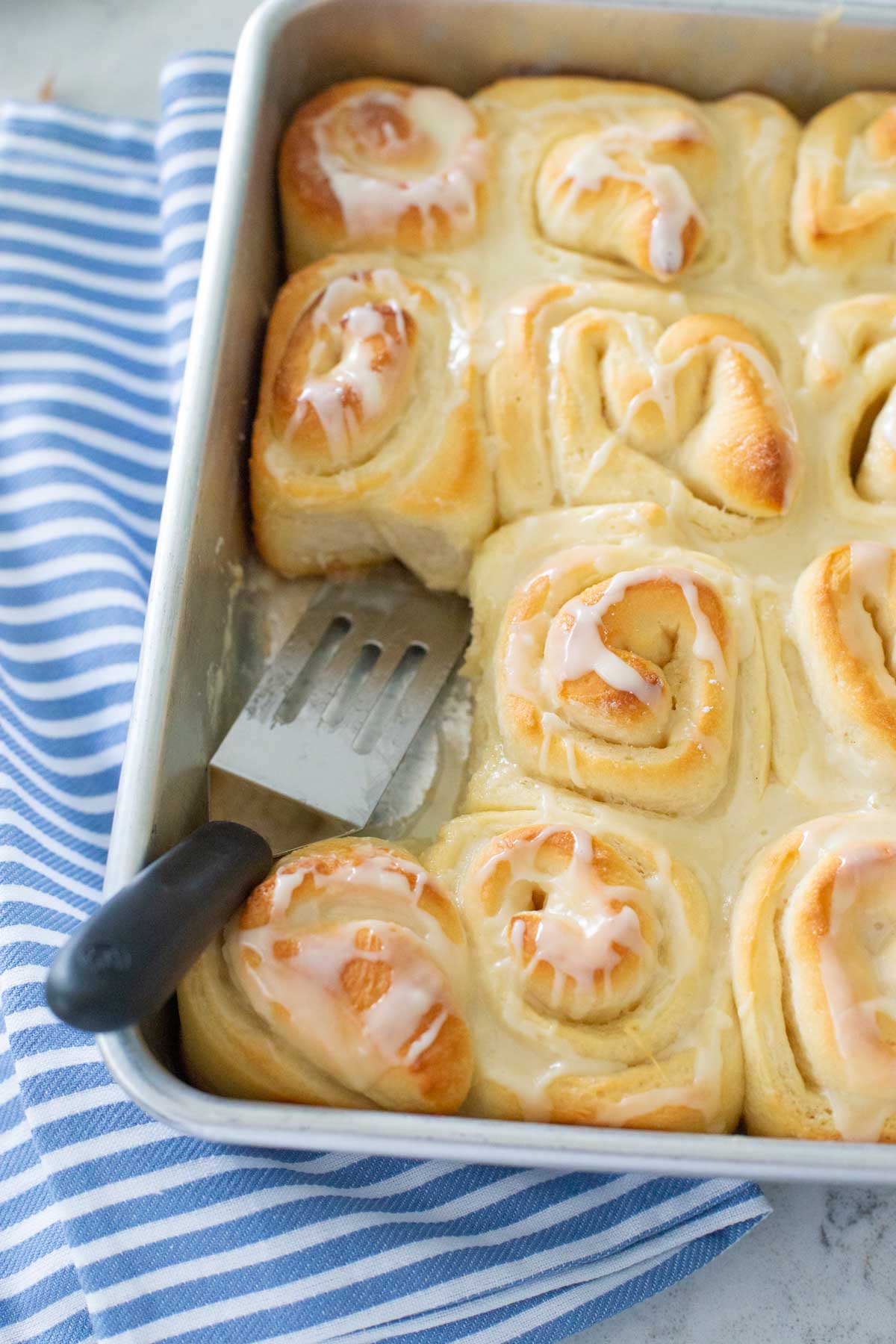 The orange rolls have been iced and a spatula is serving one.