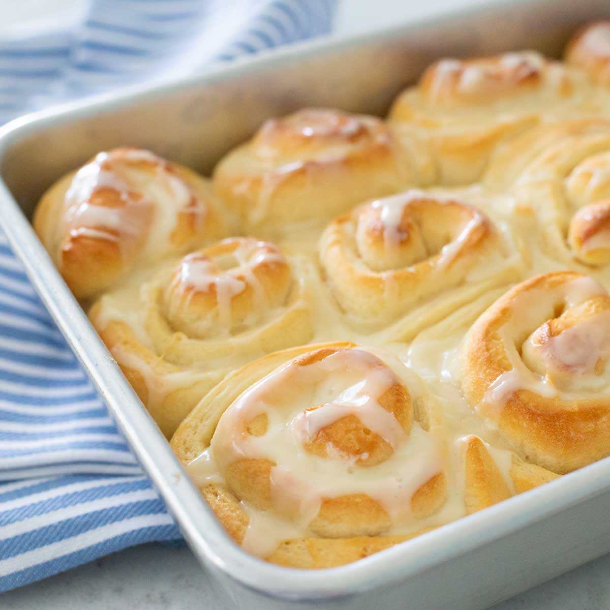 A baking pan filled with finished orange rolls sits on a blue towel.