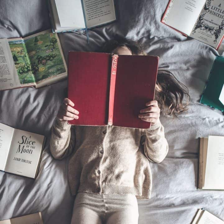 A girl lays on a bed reading a book.