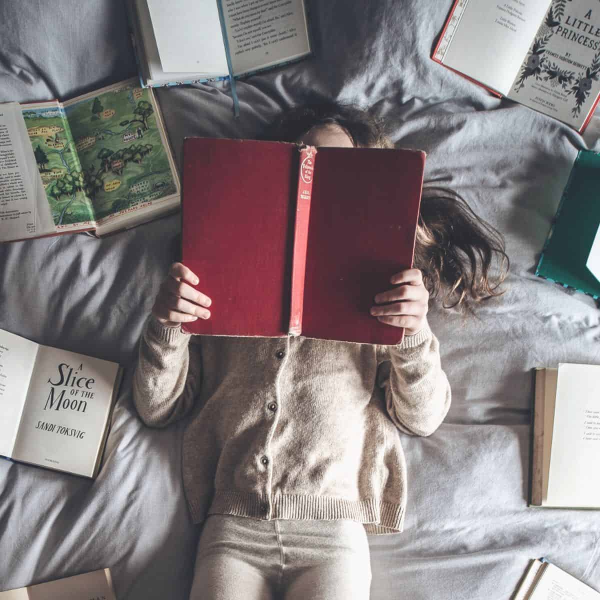 A girl lays on a bed reading a book.