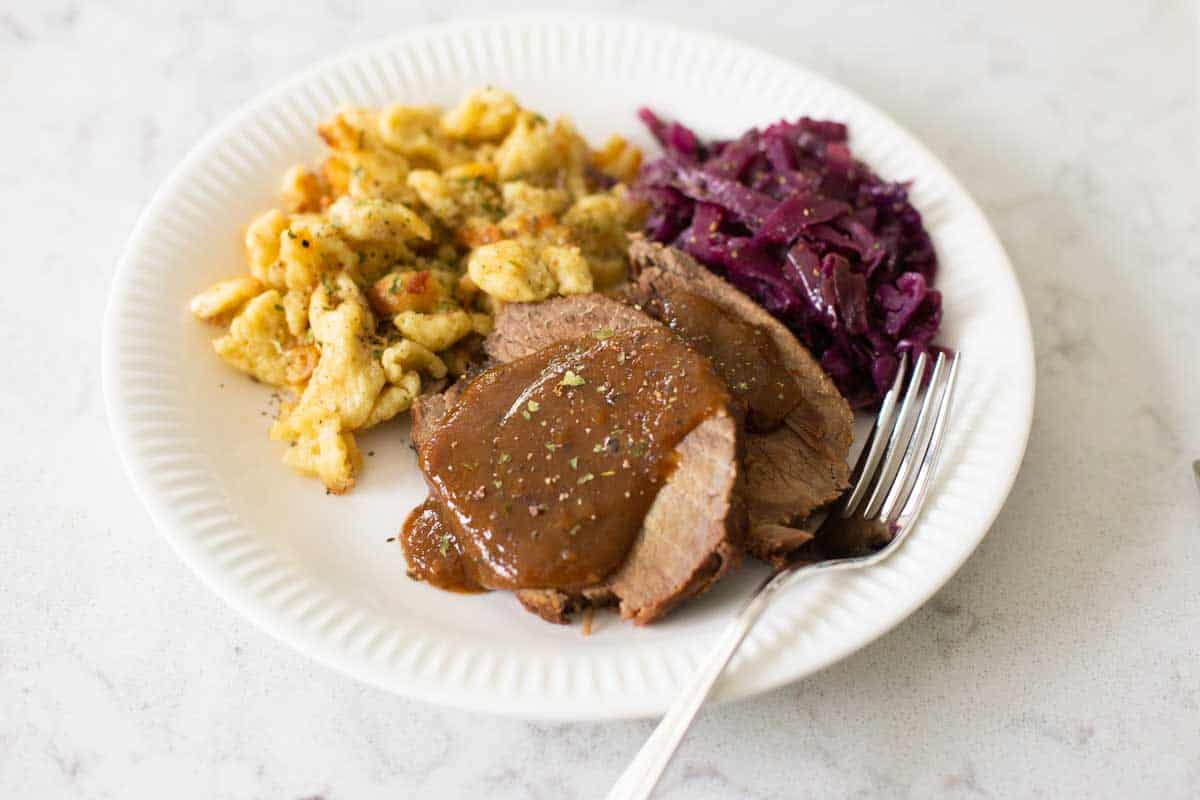 A plate of sauerbraten with spaetzle and red cabbage.