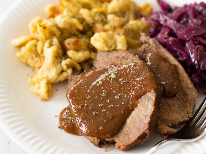 A plate of sauerbraten has homemade spaetzle and red cabbage on the side.