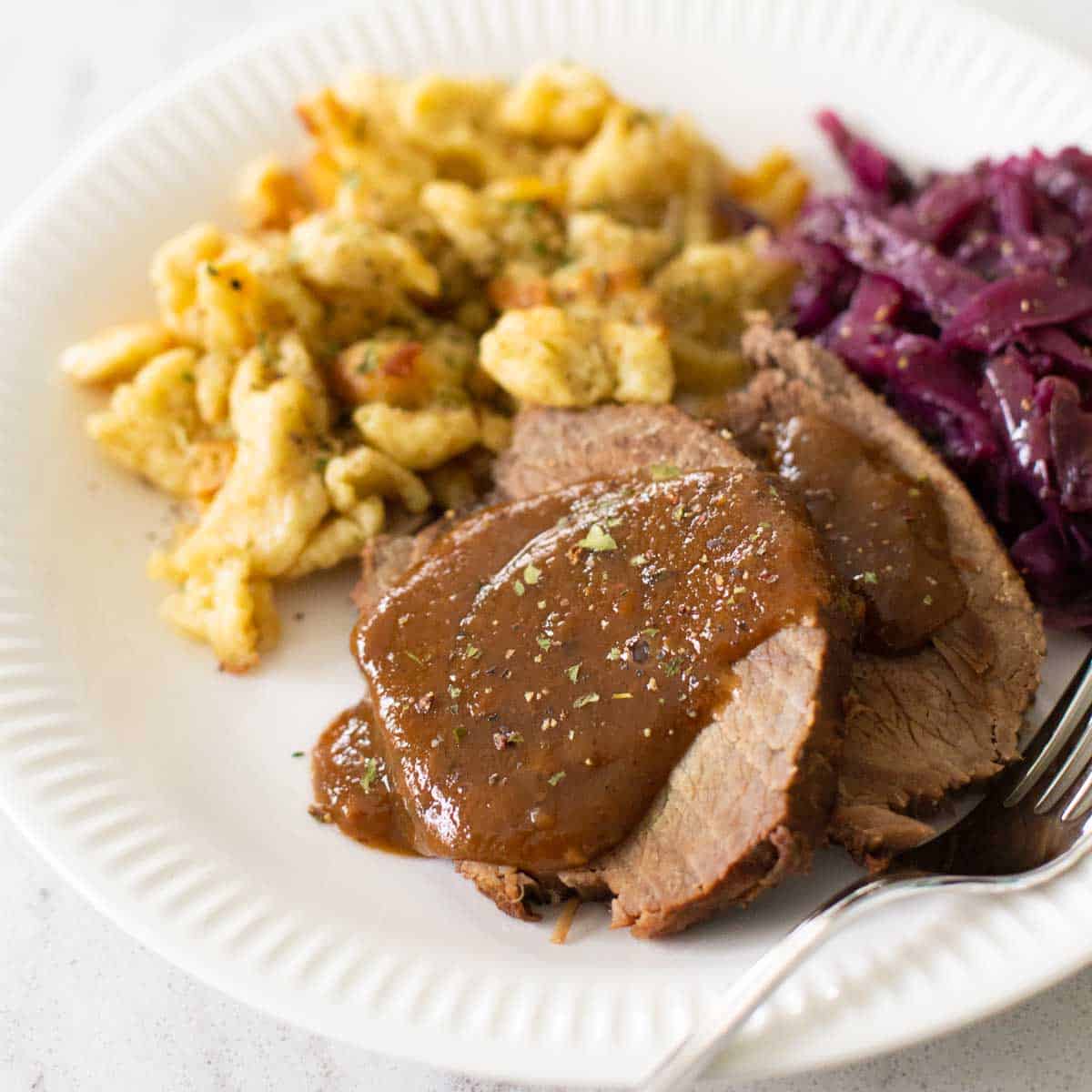 A plate of sauerbraten has homemade spaetzle and red cabbage on the side.