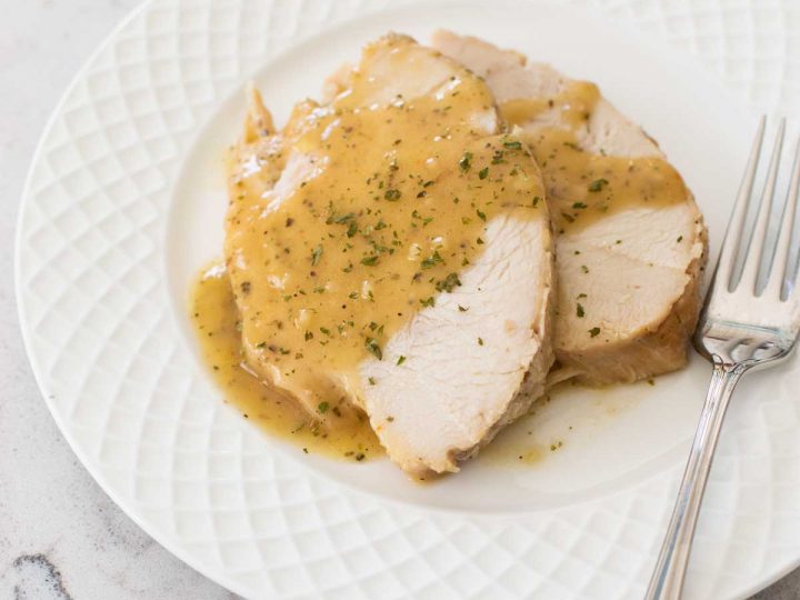 Two slices of slow cooked turkey breast are on a plate drizzled with gravy.