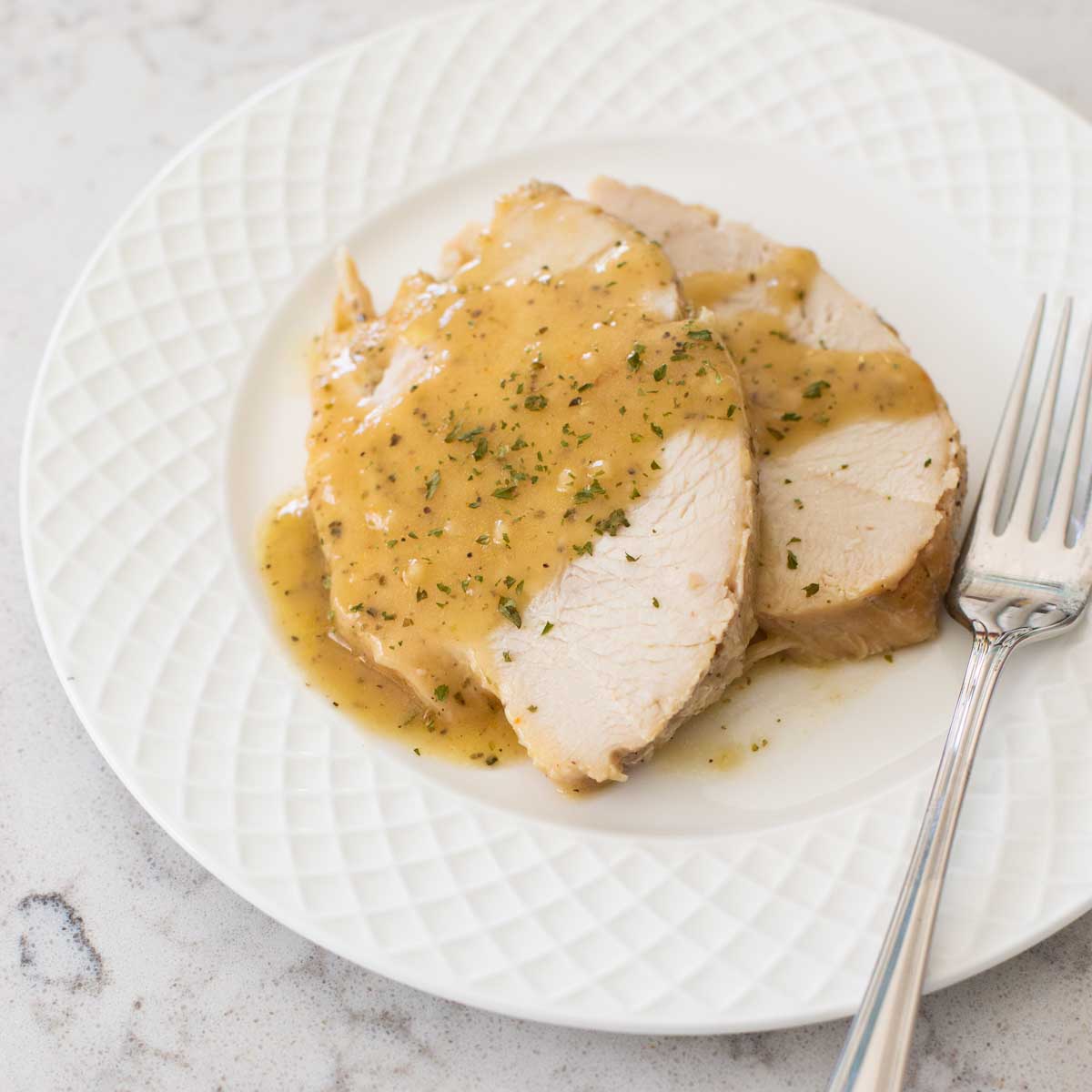 Two slices of slow cooked turkey breast are on a plate drizzled with gravy.