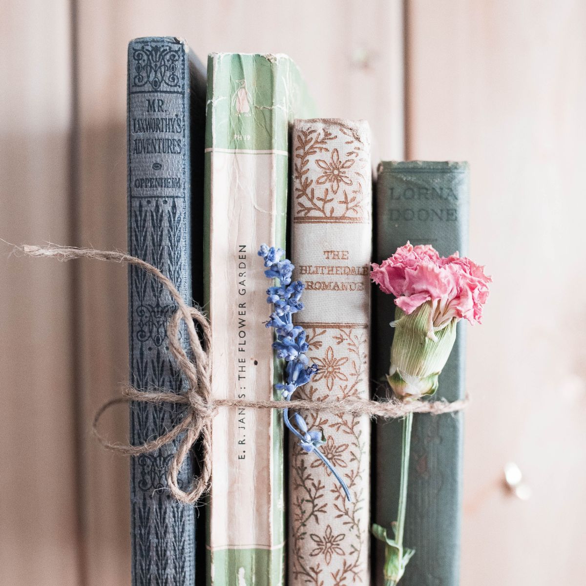 A bundle of books tied with twine has a pink carnation tucked in.