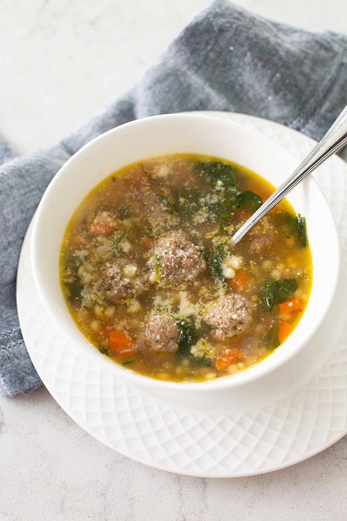 A bowl of soup has meatballs, couscous, and carrots with spinach in chicken broth.