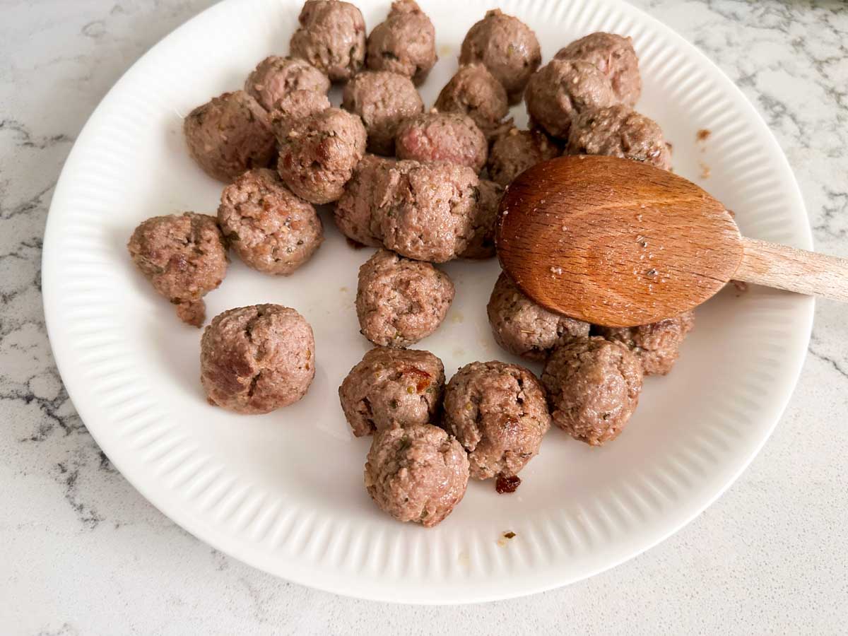 The meatballs are resting on a clean plate after being browned.