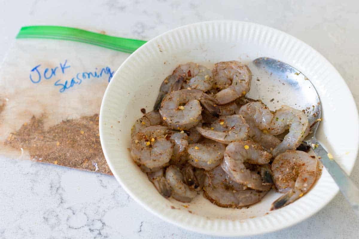 The raw shrimp are in a bowl next to a bag of seasoning.