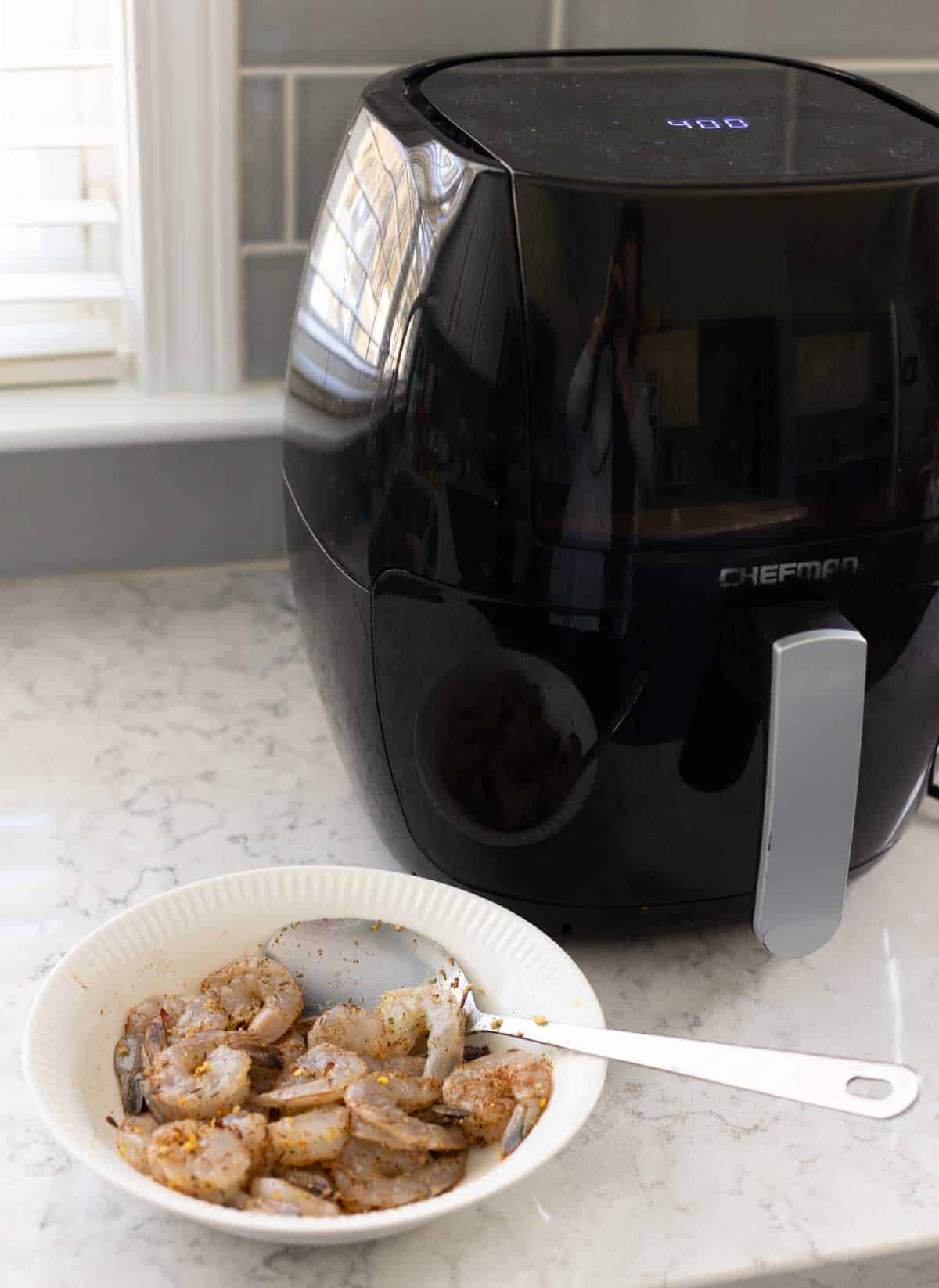 The air fryer is on the counter next to the bowl of prepared shrimp.