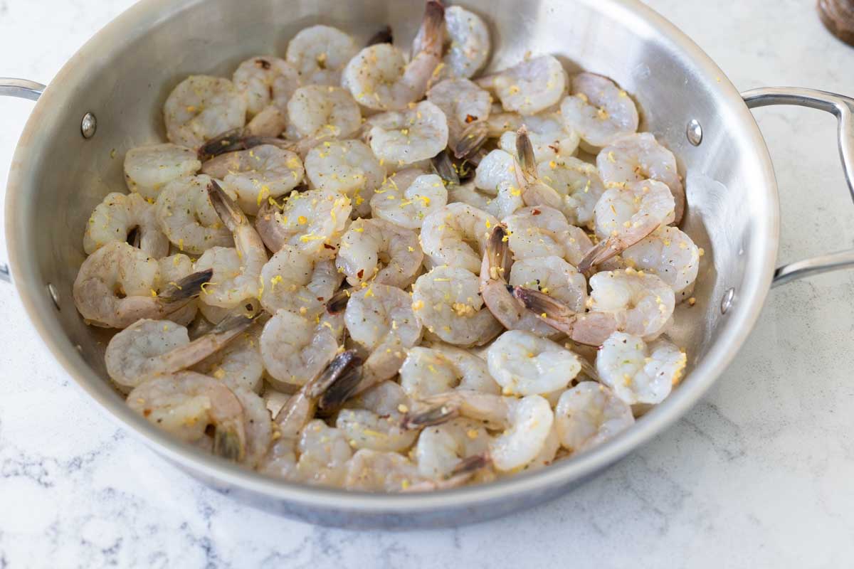 The raw shrimp have been added to a large skillet in a single layer.