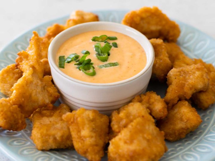 The bang bang sauce is in a dipping cup on a plate, surrounded by chicken nuggets.