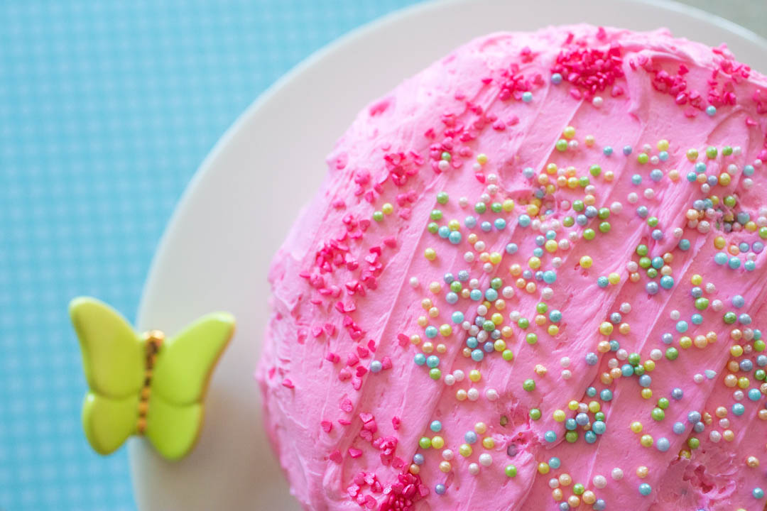 A homemade birthday cake has pink frosting and sprinkles over the top.
