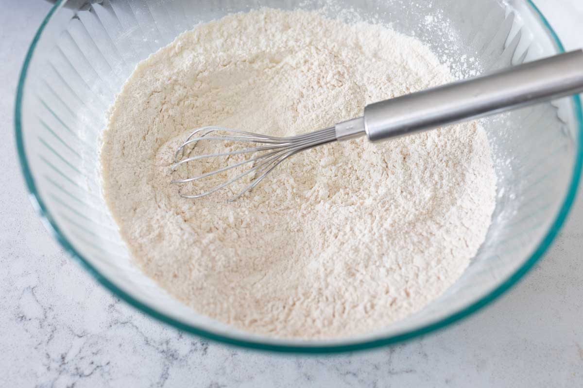 The mixing bowl has flour, sugar, and all the dry ingredients with a whisk.