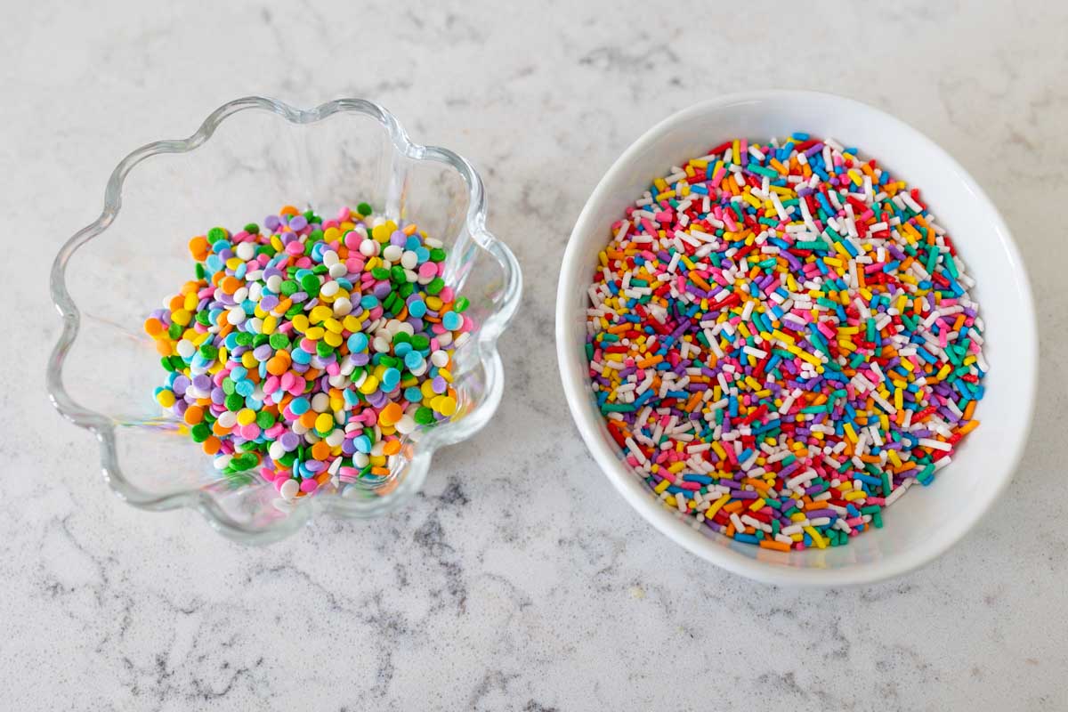 A bowl of pastel sprinkles vs. a bowl of rainbow jimmies show the difference in size and shape.