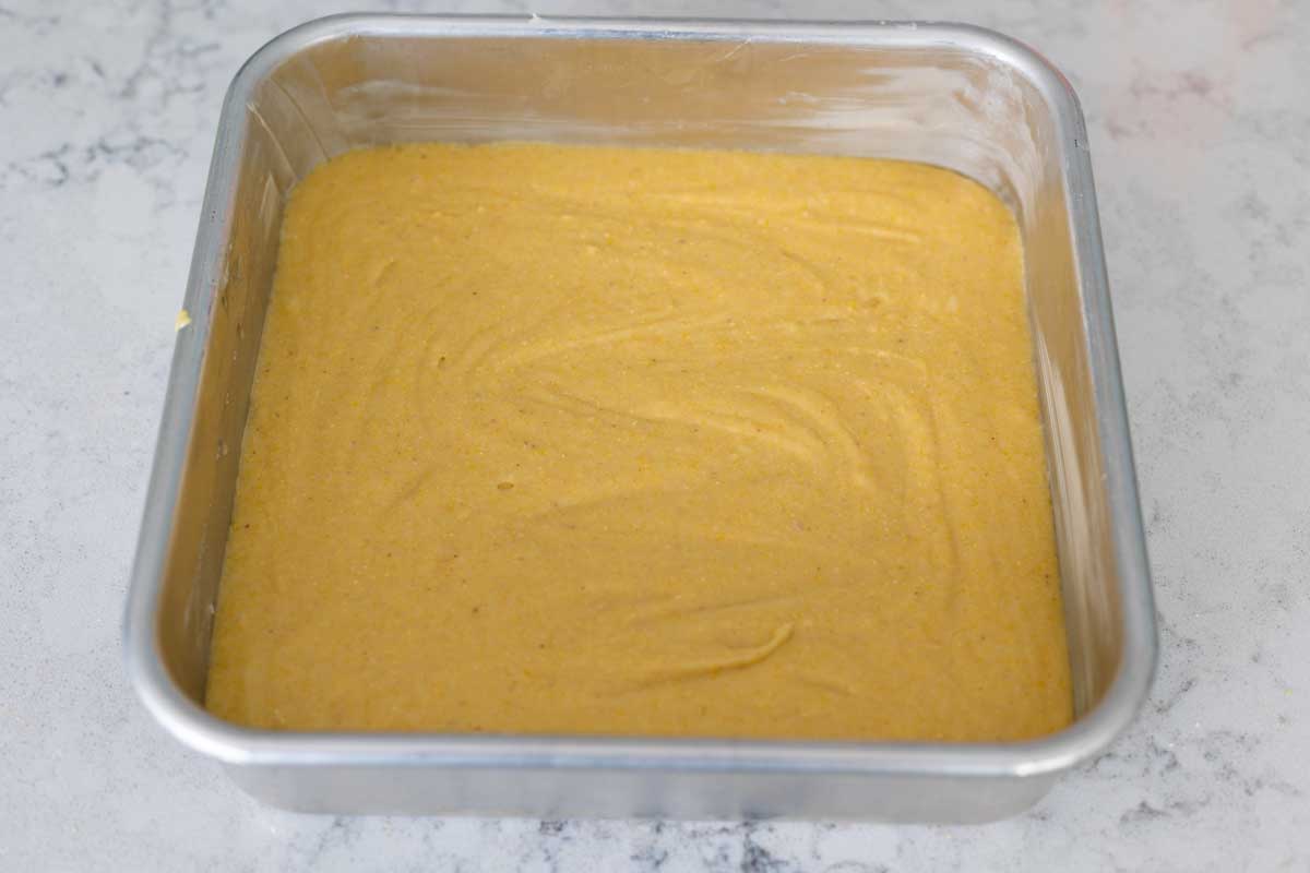 The square baking pan has cornbread batter smoothed over evenly.