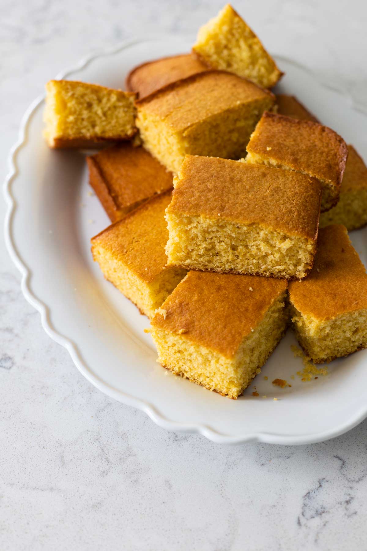 The large squares of buttermilk cornbread are served on a white ruffled platter for dinner.