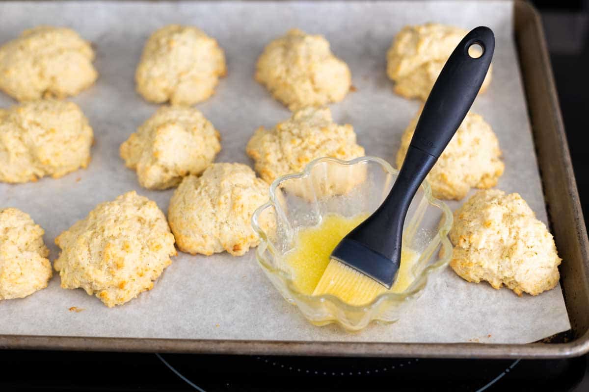 The biscuits have been baked and brushed with butter. A pastry brush in a cup of butter on the side.