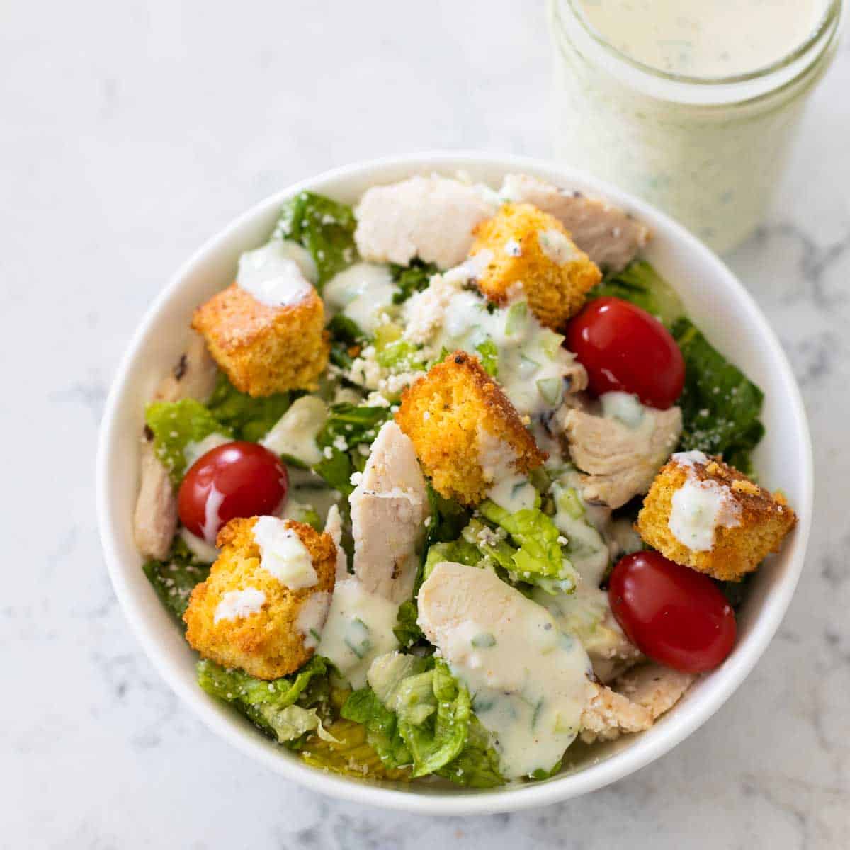 A green salad with chicken, tomatoes, and croutons has been drizzled with the buttermilk herb dressing.