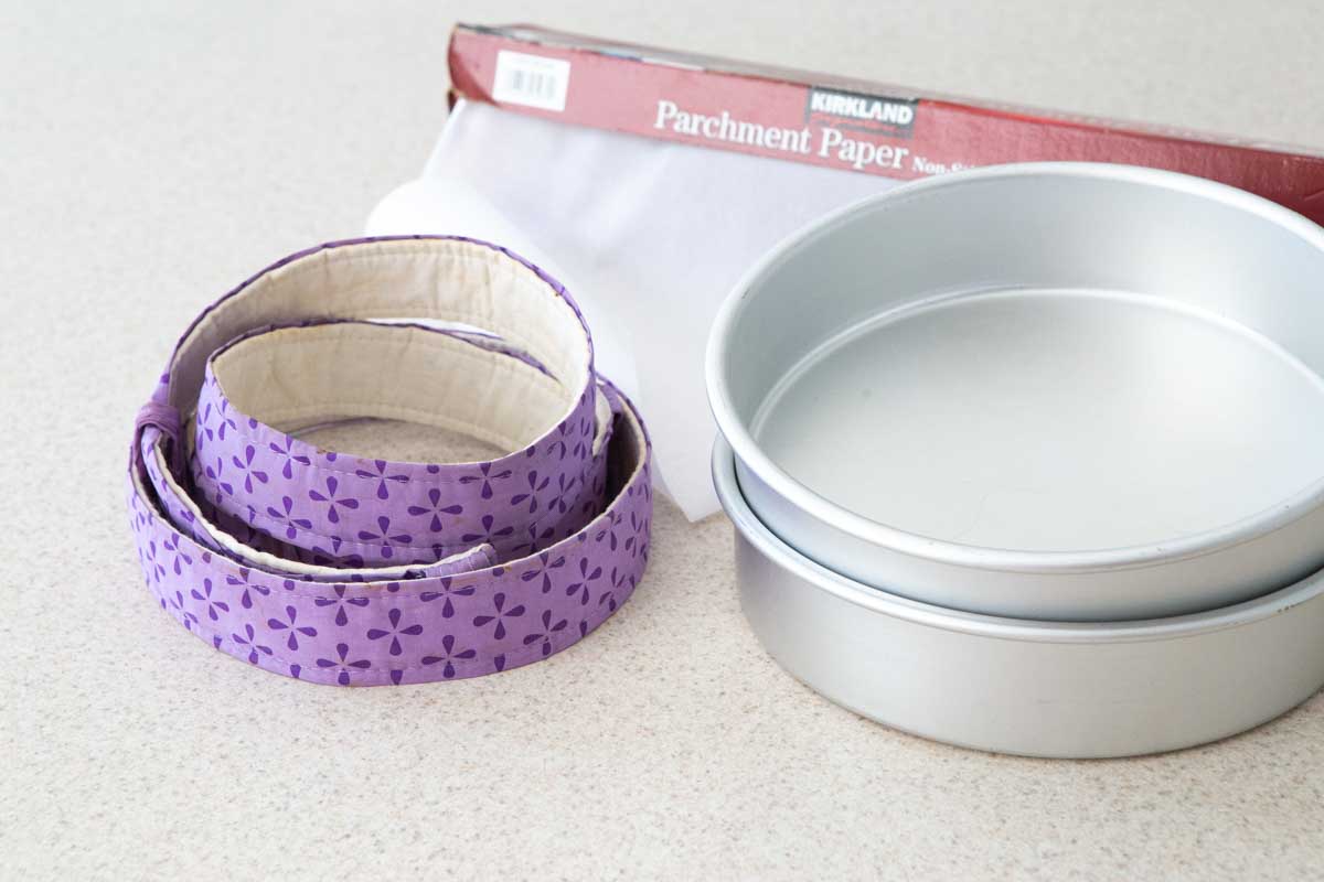 A pile of cake pans, cake strips, and parchment paper.