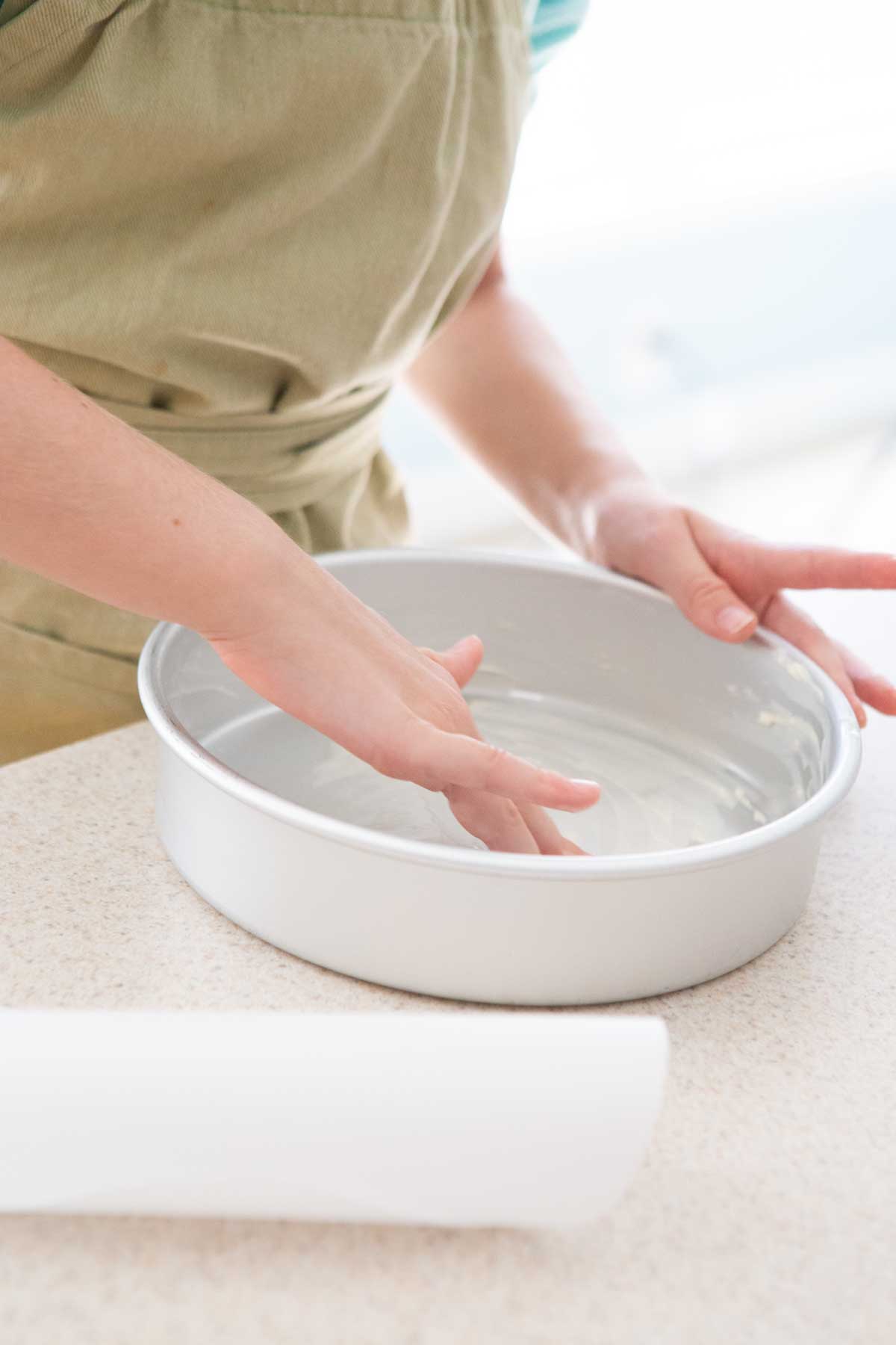 A girl rubs softened butter inside the round cake pan.