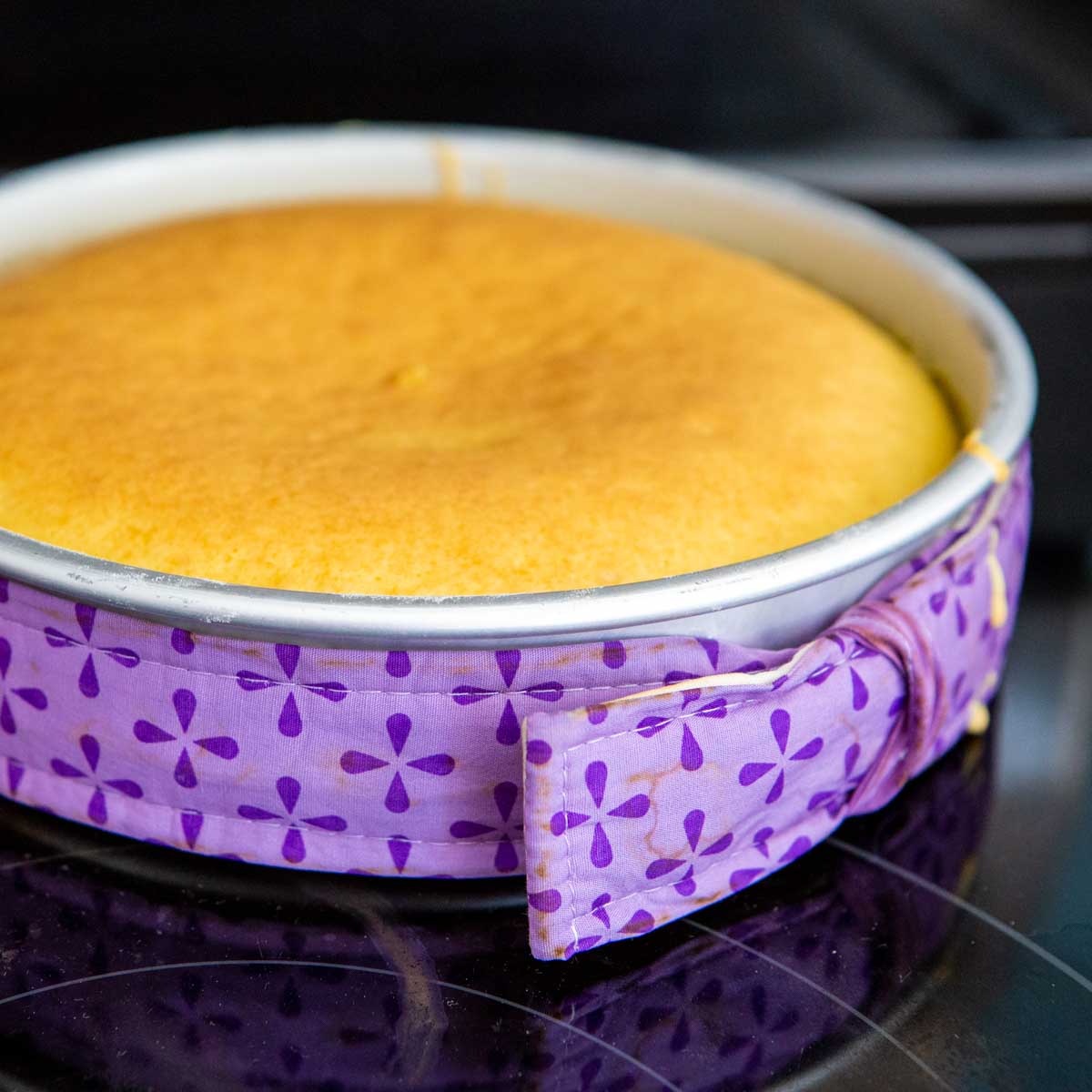 A cake pan is wrapped in a purple fabric cake strip and has a perfect level cake layer baked inside.