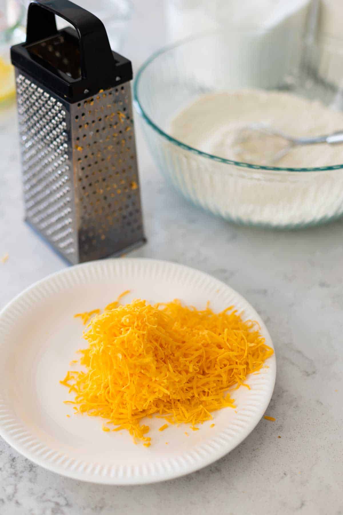 A box grater sits next to a plate of fresh shredded cheese.