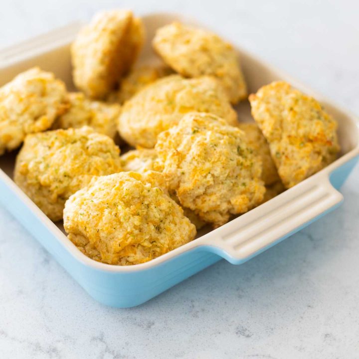 A blue dish has a batch of baked cheddar drop biscuits.