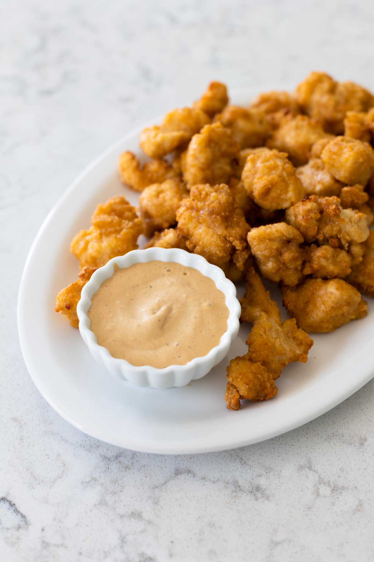 The sauce is in a cup on a platter of chicken nuggets.