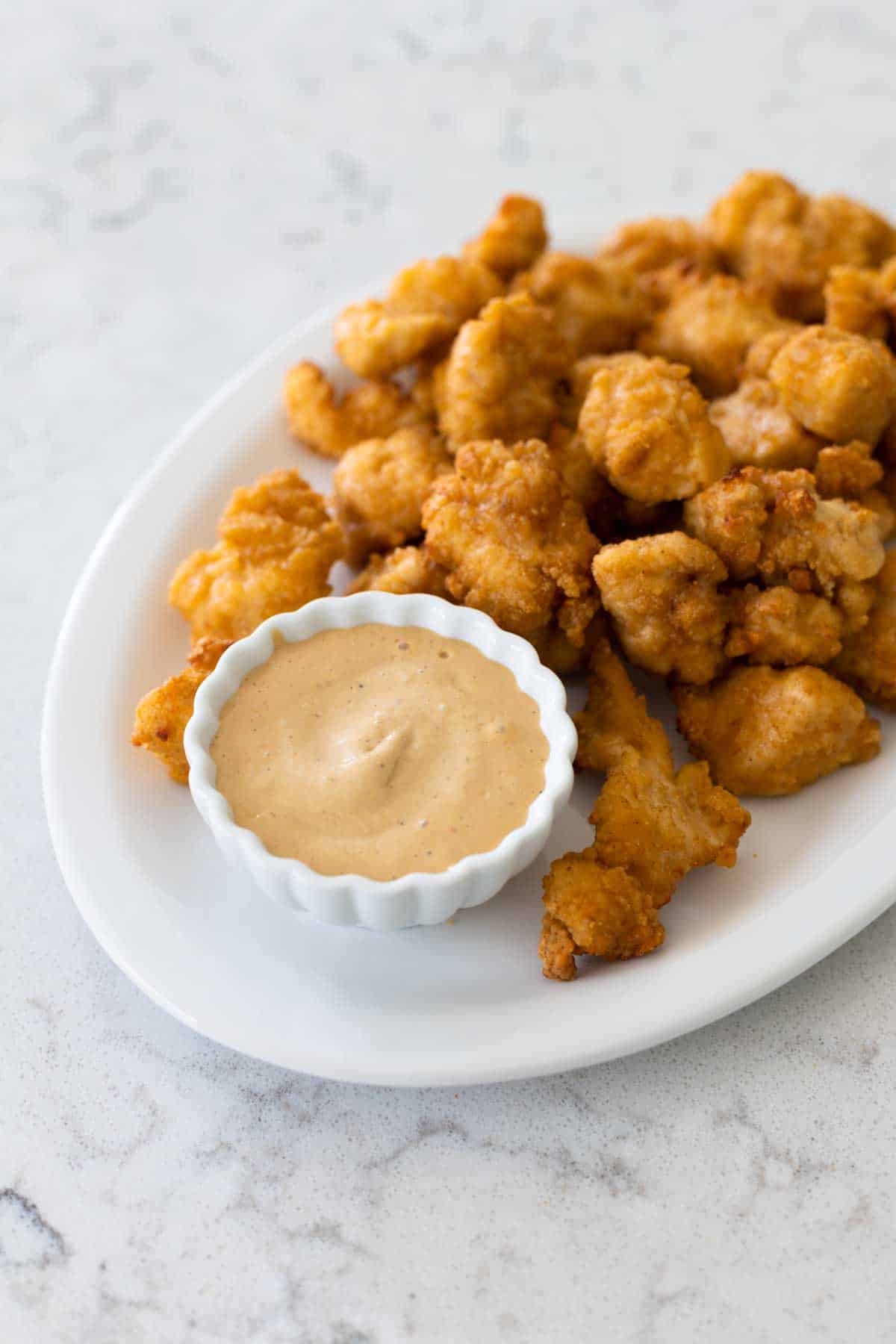 The sauce is in a cup on a platter of chicken nuggets.