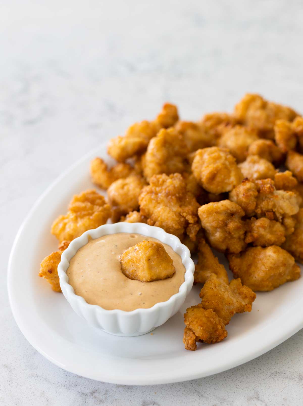 The cup of Chick-Fil-A Sauce has a chicken nugget being dunked in it. The cup rests on a platter of chicken nuggets.