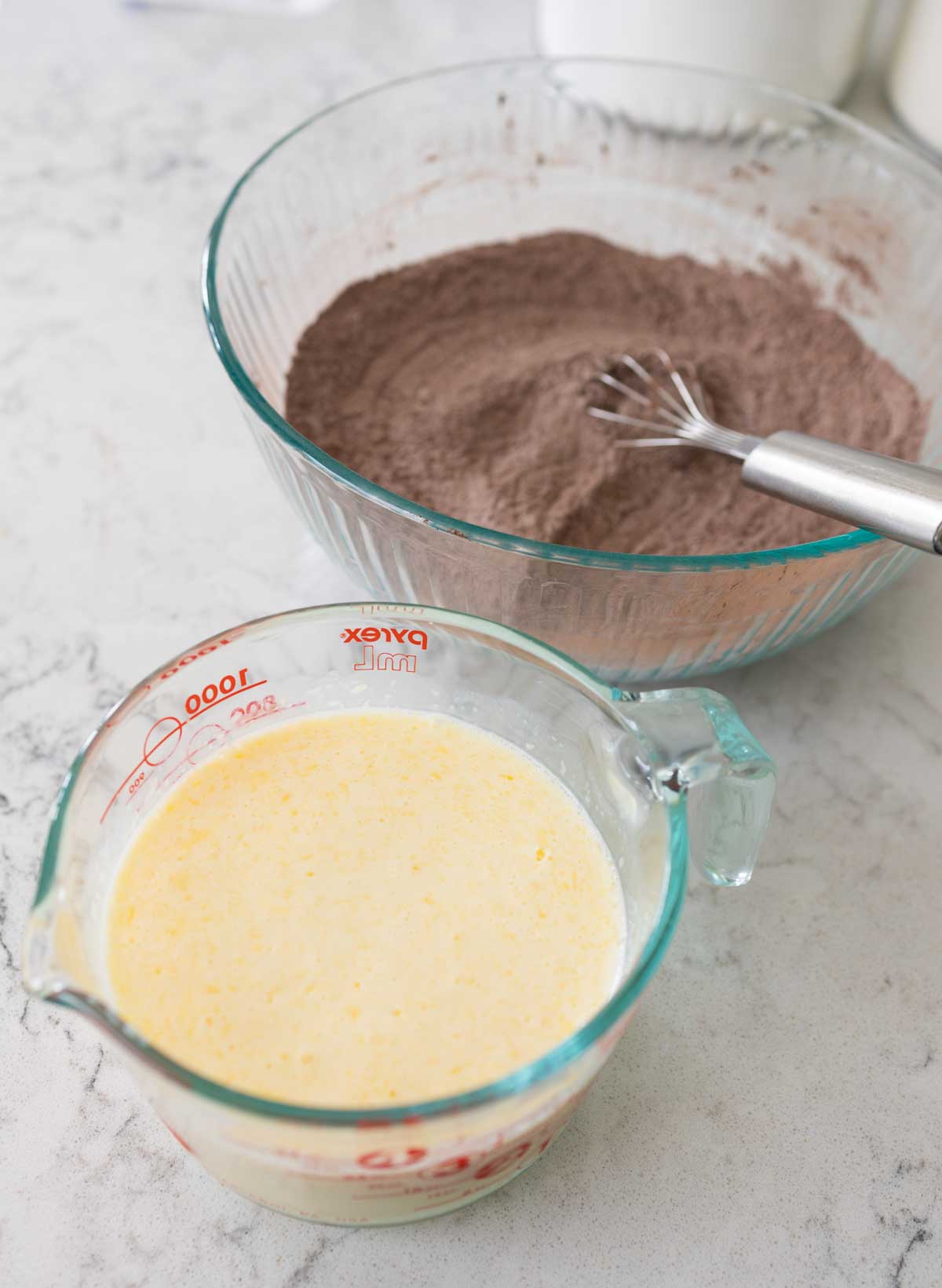 The whisked bowl of buttermilk and eggs sits next to the bowl of dry chocolate powder and flour.