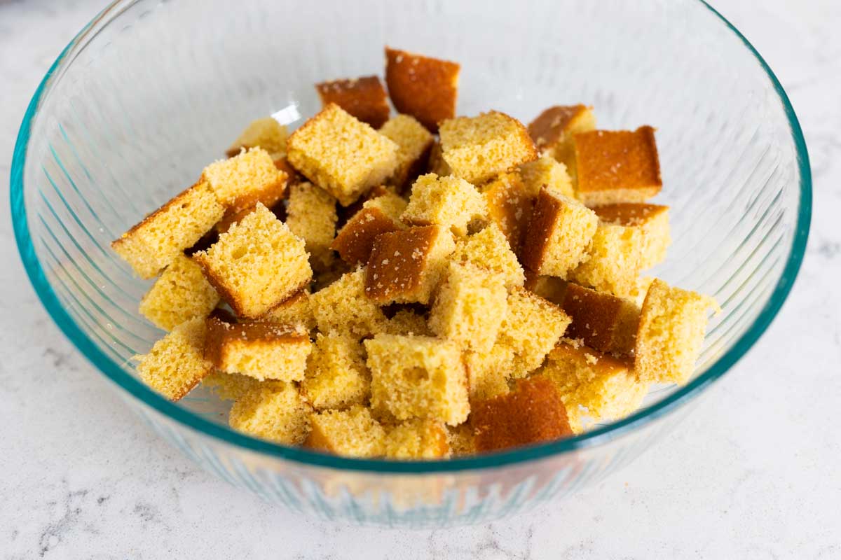 A mixing bowl is filled with cornbread that has been cut into cubes.