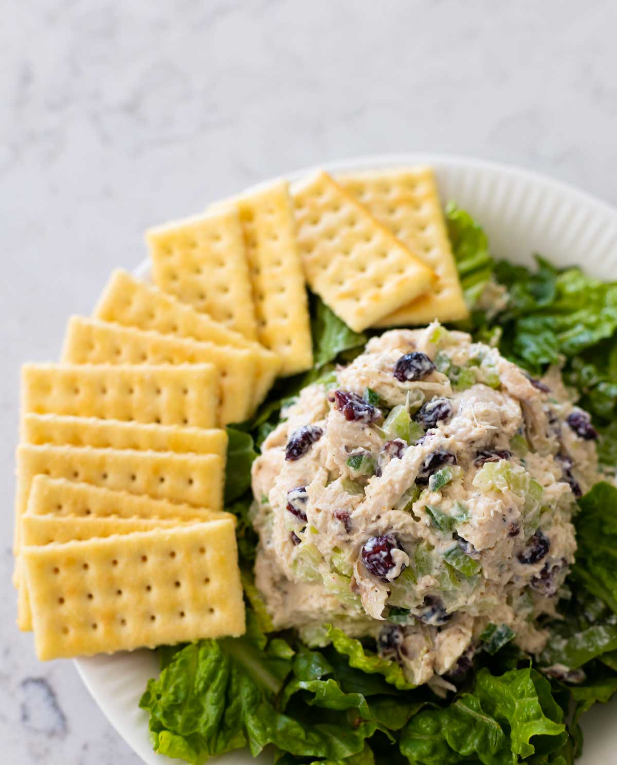 The ball of chicken salad is being served on lettuce with a plate of crackers.