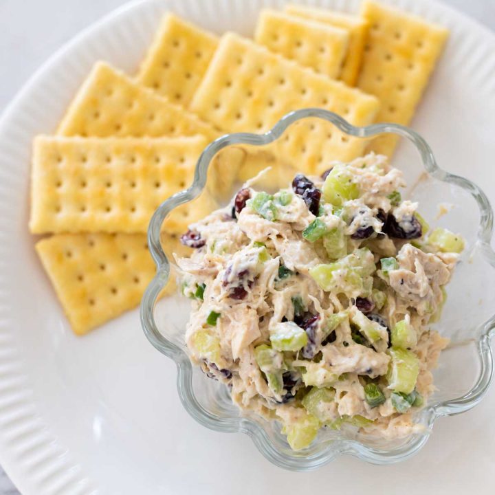 A small scoop of chicken salad is in a bowl next to a plate of crackers.