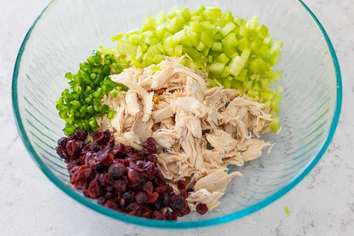 The shredded chicken, dried cranberries, minced jalapeno, and diced celery are in a large mixing bowl.