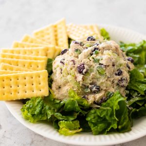 A ball of cranberry jalapeno chicken salad sits on a bed of lettuce with clubhouse crackers on the side.