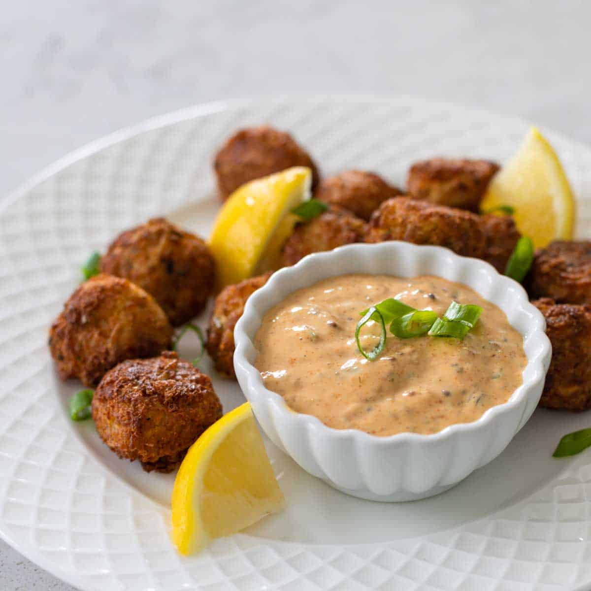 The finished sauce is in a cup on a plate of mini crab cakes with lemon wedges.