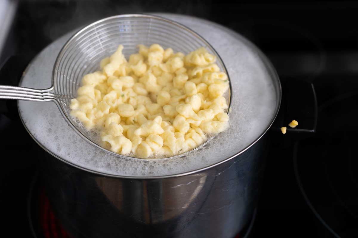 A wire spoon is straining the dumplings from the pot.