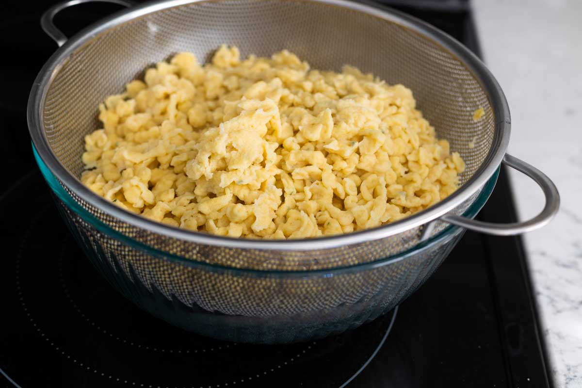 The strained spaetzle are draining in a colander over a bowl.