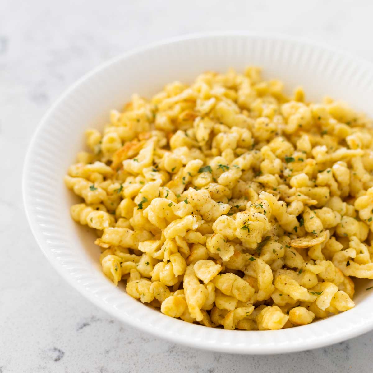 A white bowl filled with homemade spaetzle sprinkled with parsley.
