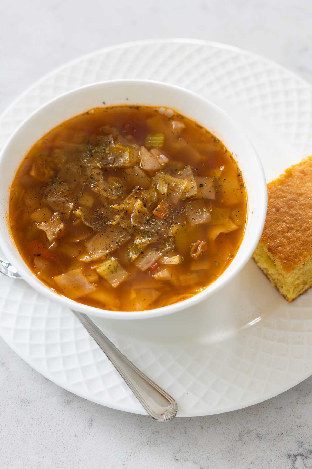The sweet and sour cabbage soup is in a white soup bowl with a piece of cornbread on the side.